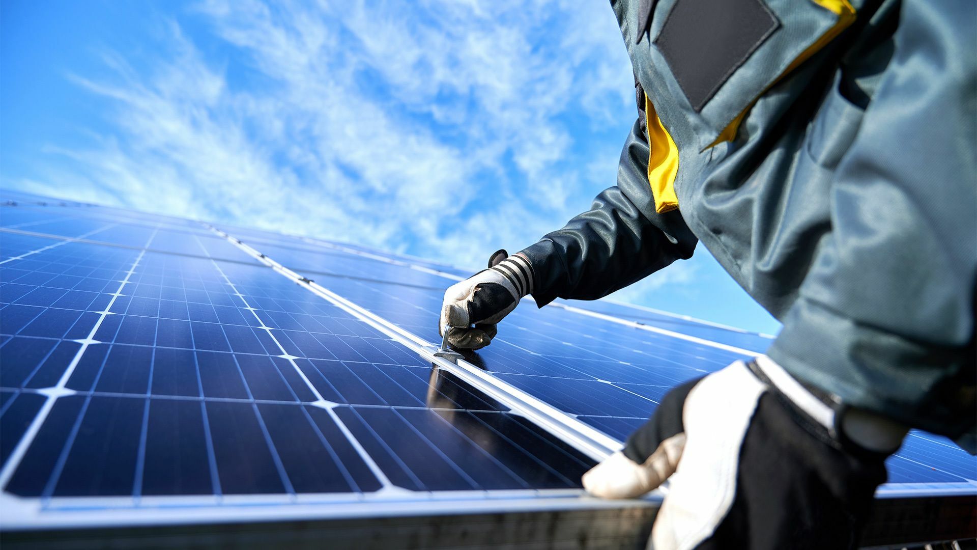 Nahaufnahme von Händen eines Technikers in Arbeitshandschuhen, der an einer Photovoltaik-Anlage arbeitet